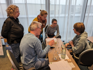 fünf Personen sitzen um einen Tisch, auf dem Gläser mit und ohne Milch stehen